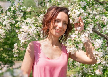 Güzel bir kadın çiçek açan bir bahçede yürüyor. Koyu saçlı bir kadının portresi. Elma ağacı baharda açar.