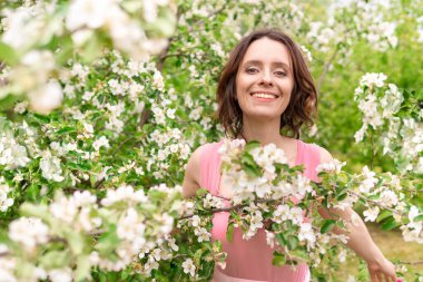 Güzel bir kadın çiçek açan bir bahçede yürüyor. Koyu saçlı bir kadının portresi. Elma ağacı baharda açar.