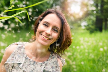 Güneşli bir günde çimenlerde oturan bir kadının portresi. Parkta bir kız yürüyor. O mutlu..