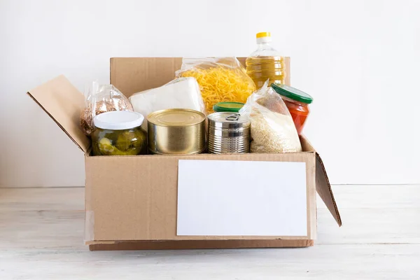 Cardboard box with butter, canned food, cereals and pasta. A donation box with various food items.