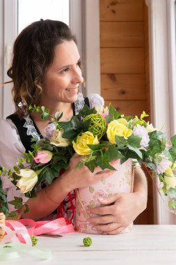 Elinde bir demet kağıt çiçekle bir kadın pencerede duruyor..