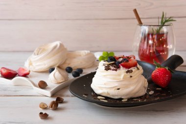 Çilekli bir tabakta beyaz tatlı ve açık ahşap bir masada bitki çayı.