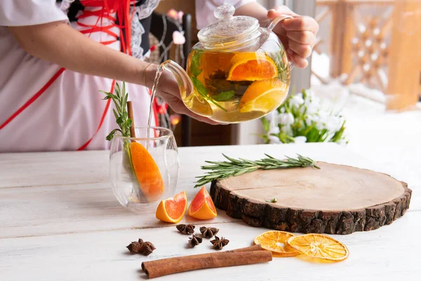 A glass teapot with healthy herbs and fruits. Women\'s hands pour tea.