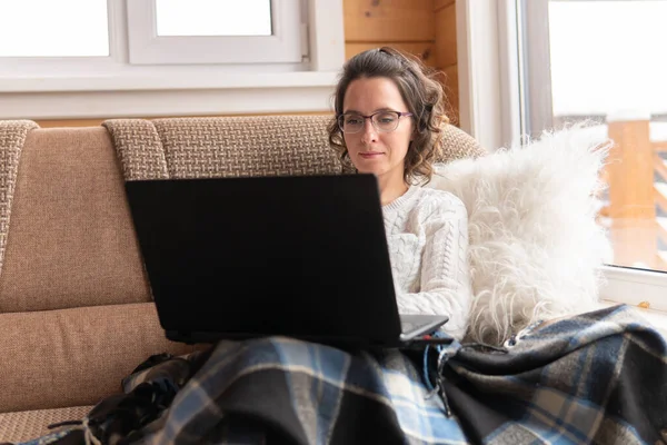 Woman with laptop working at home on the couch. She communicates on the Internet. She covered herself with a veil.