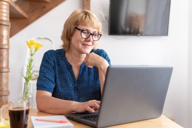 Masada çalışan orta yaşlı bir kadın laptop ekranına bakıyor. Haberleri okuyor ve sosyal ağları izliyor..