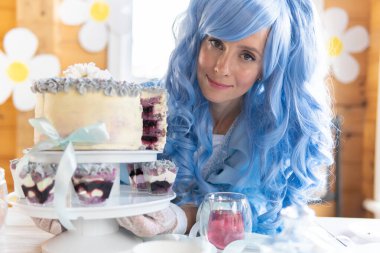 Mavi peruklu, peri kostümlü bir kadın elinde bir pasta tutuyor..