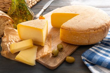 Ahşap bir arka planda, domates ve bitkilerle birlikte bir parça peynir..