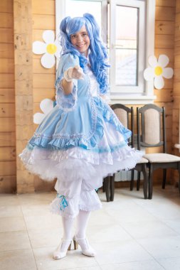 Mavi peruklu, peri masalı kostümlü bir kadın elini ileri uzatıyor..