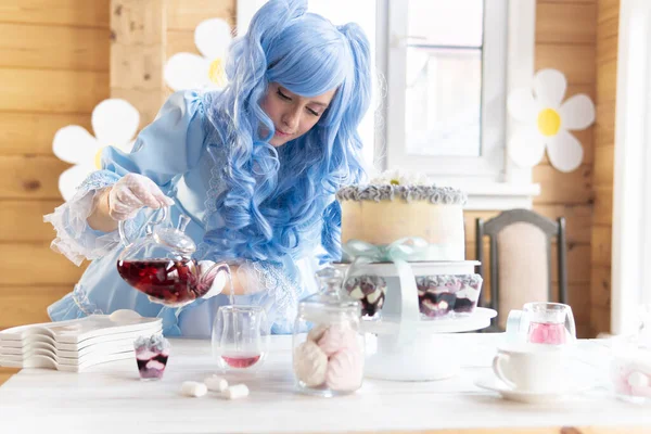 Mavi peruklu, peri kostümlü bir kadın çaydanlıktan çay dolduruyor.