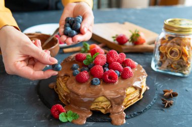 Çikolata kremalı krep ve koyu mavi arka planda kırmızı böğürtlen. Yemeği kadın elleri süslüyor..