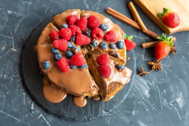 Krepten yapılmış, çikolata kremalı ve koyu mavi arka planda kırmızı dutlu kek..