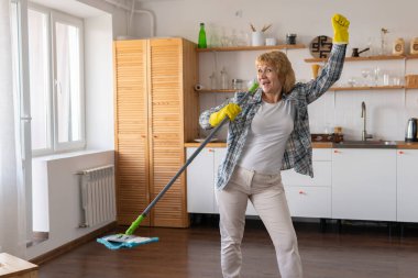Elinde paspas olan bir kadın mutfağı temizliyor..