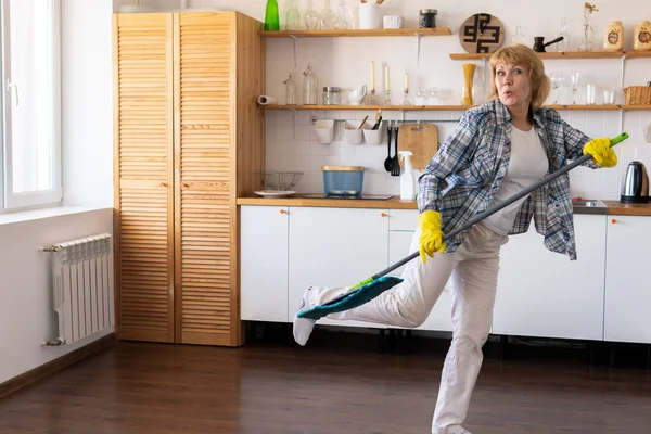 Una mujer con una fregona limpia la cocina. — Foto de Stock