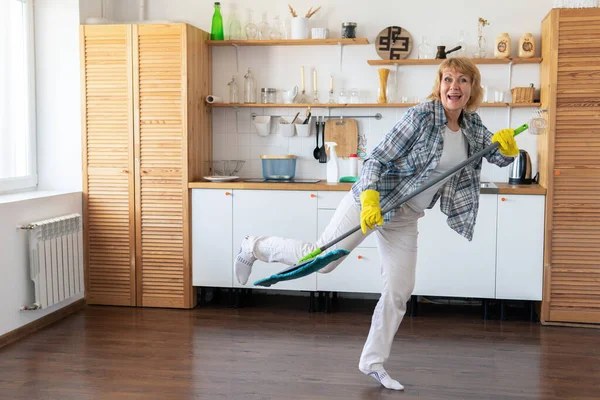 Una mujer con una fregona limpia la cocina. — Foto de Stock