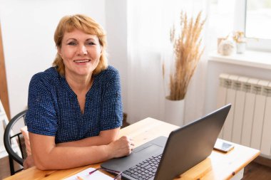 Bir kadın bir masada dizüstü bilgisayarla oturuyor..