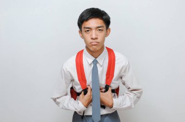 Gri arka planda izole edilmiş, üniformalı, tembel Asyalı lise öğrencisinin portresi.