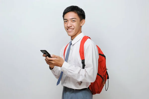 高校生インドネシアの制服を着た学生がカメラを見て笑顔で携帯電話を持ち 灰色の背景に隔離された — ストック写真
