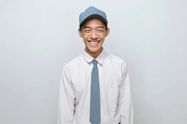 Kameraya gülümseyen üniformalı yakışıklı lise öğrencisi, gri arka planda soyutlanmış.