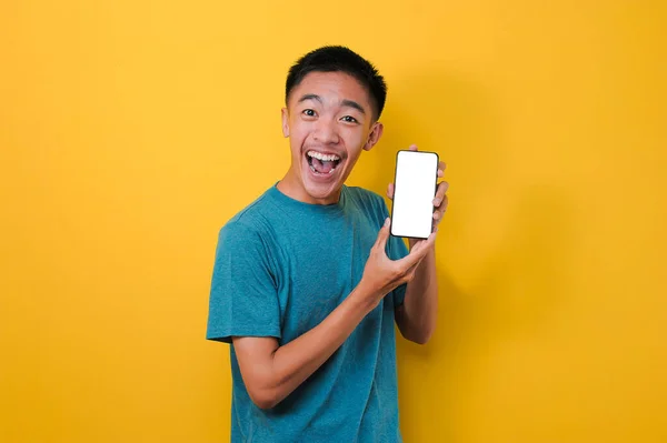 兴奋的年轻亚洲男子震惊地在摄像机前展示白色手机屏幕 被黄色背景隔离 — 图库照片