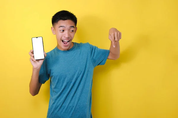 아시아 남자가 노란색 배경에 카메라로 공간을 가리키며 핸드폰 화면을 — 스톡 사진