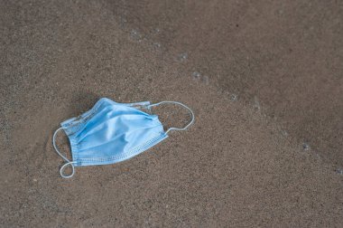 Plajda duran tek kullanımlık mavi tıbbi maske. Sahildeki kumsalda koruyucu yüz maskesi. deniz ve okyanus kirliliği