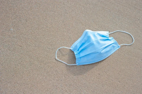 海岸に横たわる使い捨ての青い医療用マスク 海岸の砂の上の保護面 海と海の汚染 — ストック写真