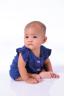 Beyaz arka planda, beyaz zeminde oturan sevimli küçük kız.