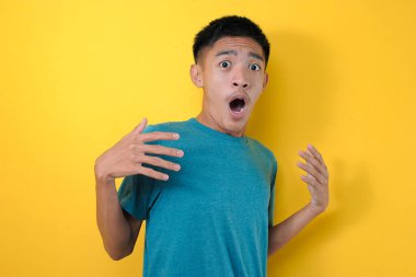 Şok olmuş genç Asyalı bir adam sıradan bir gömlek giyiyor ve çok duygusal ve şaşırmış görünüyor, sarı arka planda soyutlanmış.