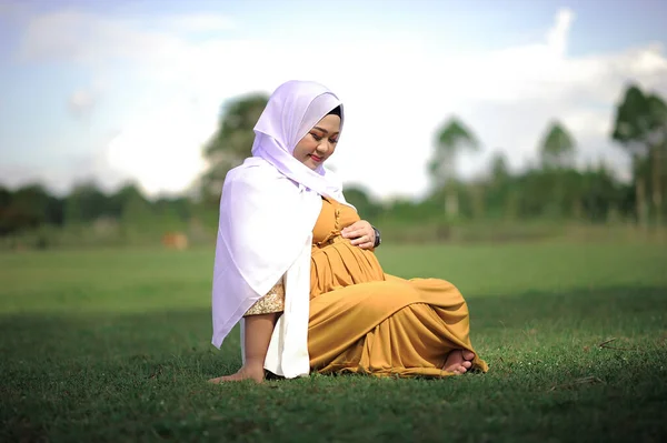 Hamile Asyalı Müslüman kadın parkta dinleniyor.