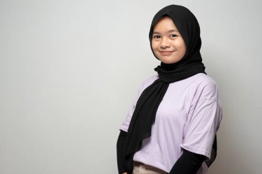 Beautiful Asian Muslim teenager with headscarf standing smiling at the camera, isolated on grey