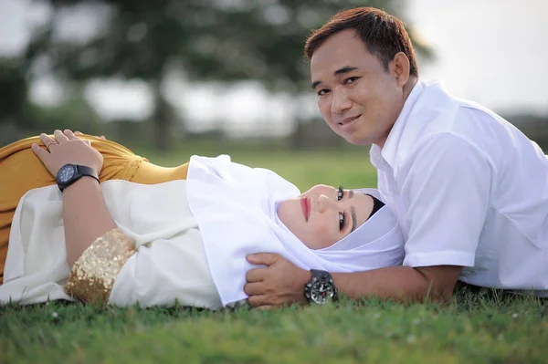 Husband and Pregnant Wife Laying on Grass. Couple Muslim maternity photo. Fun in grass