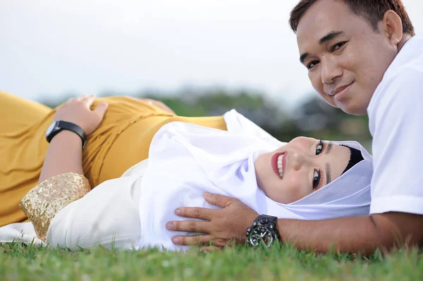 Husband and Pregnant Wife Laying on Grass. Couple Muslim maternity photo. Fun in grass