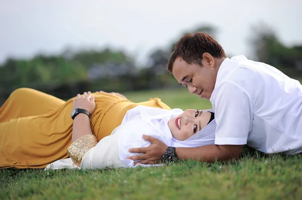 Husband and Pregnant Wife Laying on Grass. Couple Muslim maternity photo. Fun in grass