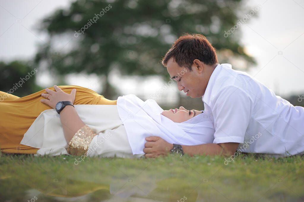 Husband and Pregnant Wife Laying on Grass. Couple Muslim maternity photo. Fun in grass