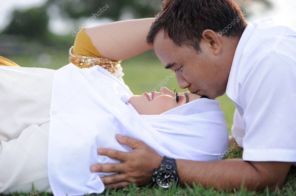 Husband and Pregnant Wife Laying on Grass, Close up a Husband kiss his wife's forehead. Couple Muslim maternity photo. Fun in grass