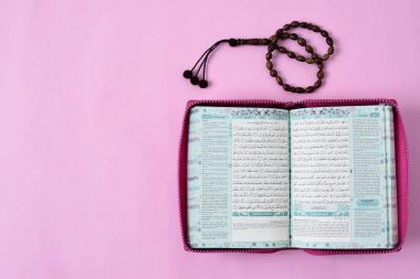 Kota Bangun, Endonezya. 29 Nisan 2021 'de Müslümanların kutsal Kur' an 'ı ve pembe arkaplan renginde tespih boncuklarının üst görünümü