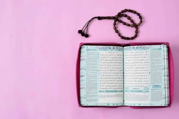 Kota Bangun, Endonezya. 29 Nisan 2021 'de Müslümanların kutsal Kur' an 'ı ve pembe arkaplan renginde tespih boncuklarının üst görünümü