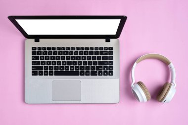 Modern kablosuz kulaklığın Top View Flatlay 'i ve pembe renkli çalışma alanı üzerinde beyaz ekranlı minimalist laptop