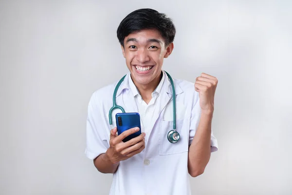 幸せな興奮若いアジアの医師男の成功は 白い背景に 携帯電話を保持するウイングジェスチャーを行う — ストック写真