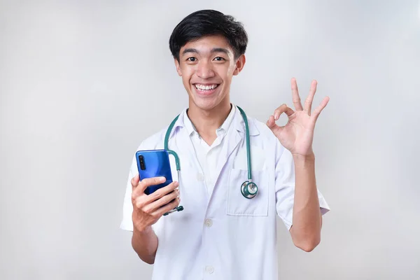 Jovem Médico Asiático Feliz Sorrindo Mostrando Sinal Segurando Telefone Celular — Fotografia de Stock