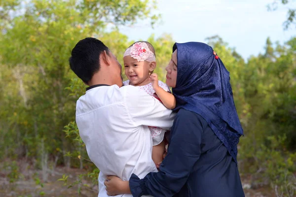 Midshot of a happy family outside on nature. Happy Young Asian Muslim mother and father hugs his daughter