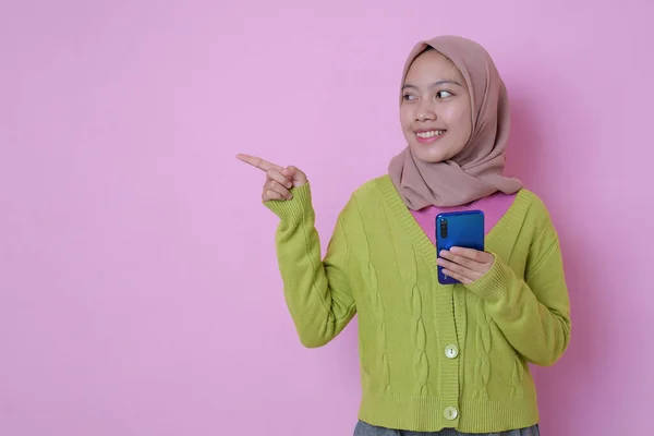 Uśmiechnięta Młoda Muzułmanka Azjatka Wskazująca Miejsce Przy Telefonie Różowym Tle — Zdjęcie stockowe