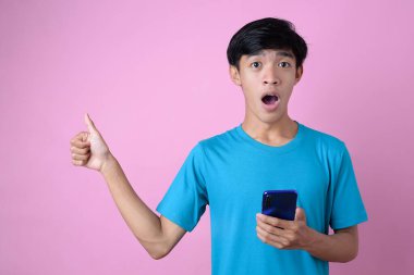 Asyalı bir adam pembe arka planda baş parmağıyla bir cep telefonunu fotokopi alanında tutuyor.