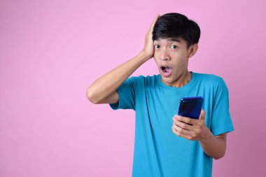 Asyalı bir adam pembe arka planda fotokopi alanı olan bir cep telefonunu tutarken şok geçiriyor.