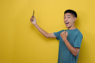 Sarı arka planda izole edilmiş akıllı telefon kullanan mutlu Asyalı adamın yan görüntüsü