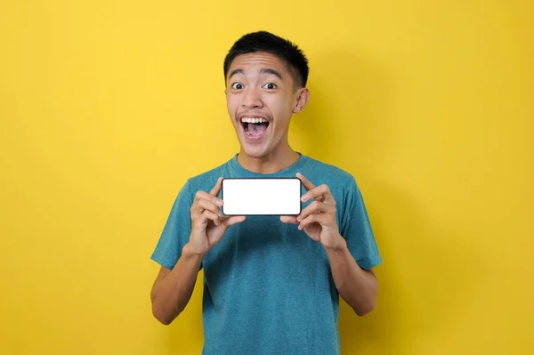 快乐兴奋的年轻亚洲男子在摄像机前展示白色手机屏幕 黄色背景隔离 — 图库照片