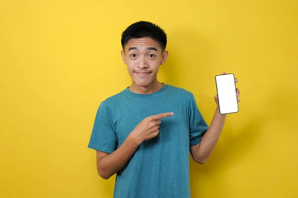 在空荡荡的智能手机屏幕上微笑着的亚洲男人 指着手机 看上去很满意 在黄色的背景下被隔离 — 图库照片
