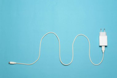 Beyaz mobil şarj cihazının üst görüntüsü, açık mavi arka planda. Enerji yönetimi ve elektrik enerjisi tasarrufu kavramı