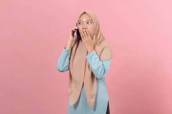 若い美しいアジアのイスラム教徒の女性はピンクの背景に隔離された手のひらで携帯電話を閉じて口でショックを受けました — ストック写真