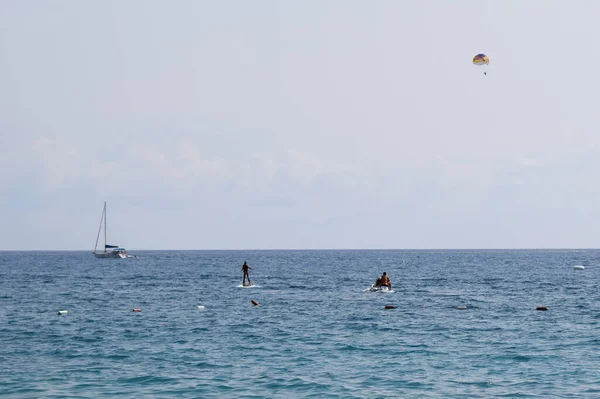 海でのフライボードライダーのシルエットと水平線上の海とセーリングボートの上に青い空にパラセーリング 水のジェットパックを使用しています 極端なウォータースポーツの概念 ジェットスキー動力フライボード — ストック写真